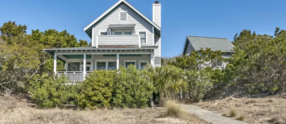 Beach cottage on a grassy dune with trees surrounding